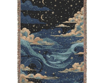 Può includere: Una coperta tessuta rettangolare con un design a cielo notturno. La coperta raffigura un cielo blu scuro pieno di stelle, lune crescenti e nuvole in tonalità di blu e beige. I bordi hanno un bordo sfrangiato.