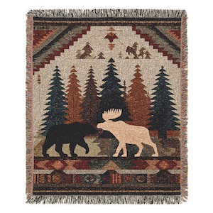 May include: Woven throw blanket with a forest scene featuring a bear and moose. The blanket has a fringed edge and a geometric pattern in shades of brown, green, and beige. The design includes trees and mountain silhouettes.