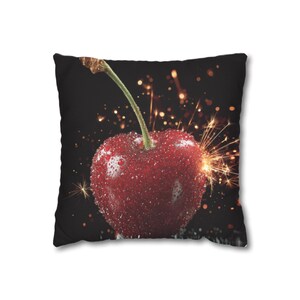 May include: Square cushion featuring a close-up of a ripe, red cherry with water droplets. The cherry has a green stem and is set against a black background with sparkling effects. A decorative accent for home decor.