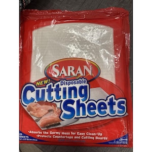 May include: A red and clear plastic package of Saran disposable cutting sheets. The package has the words "Cutting Sheets" in large blue letters. The package also says "Absorbs the Germy Mess for Easy Clean-Up" and "Protects Countertops and Cutting Boards".
