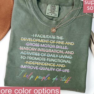May include: An olive green crewneck t-shirt featuring white text that reads: I FACILITATE THE DEVELOPMENT OF FINE AND CROSS MOTOR SKILLS, SENSORY INTEGRATION, AND ACTIVITIES OF DAILY LIVING TO PROMOTE FUNCTIONAL INDEPENDENCE AND IMPROVE QUALITY OF LIFE.
