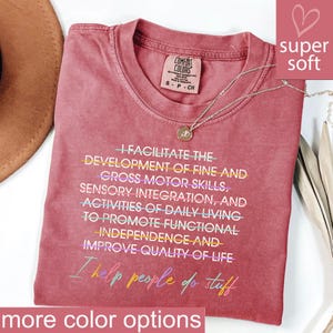 May include: A dusty rose Comfort Colors t-shirt with the text "I facilitate the development of fine and gross motor skills... I help people do stuff." A silver necklace with a pendant is draped across the shirt. The shirt is labeled "super soft."