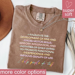 May include: A brown Comfort Colors t-shirt with the text "I facilitate the development of fine and gross motor skills..." in a colorful font. A silver necklace with a pendant is on the shirt. The words "super soft" are in a pink box.