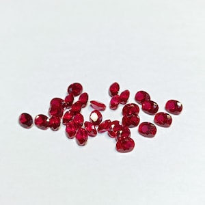 以下が含まれることがあります： さまざまなサイズの、ファセット加工された楕円形のルビーのコレクション。宝石は深く豊かな赤色で、白い表面に散らばっています。ルビーは光の反射を最大化するようにカットされており、その輝きを際立たせています。