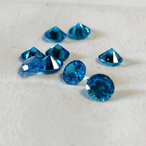 May include: Several brilliant blue gemstones with multiple facets. The gems are arranged on a white surface, reflecting light. The different shapes and sizes of the stones create a visually appealing display, highlighting their clarity and colour.
