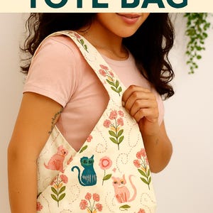May include: Cream-colored tote bag with a floral and cat pattern. The bag has a V-shaped opening and long straps. The text "SPIREA TOTE BAG" and "SEWING PATTERN WITH TUTORIAL" are printed on the image.