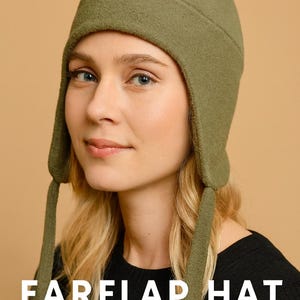 May include: An olive green earflap hat with long ties, worn by a person with blonde hair. The text "EARFLAP HAT SEWING PATTERN WITH STEP BY STEP GUIDE" is displayed below the hat. The hat is made of a soft, textured fabric.