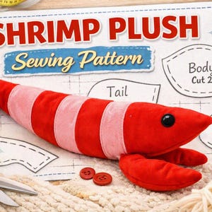 May include: A plush shrimp toy with alternating red and light pink segments, a black eye, and two front claws. It rests on a sewing pattern sheet labeled SHRIMP PLUSH Sewing Pattern, featuring outlines for body, tail, and claw pieces, with red thread.