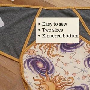 Puede incluir: Un arrullo de tela gris con ribete amarillo de lunares, con un panel central con estampado celestial de soles, estrellas y galaxias. Una tarjeta blanca muestra el texto: Easy to sew, Two sizes, Zippered bottom. Cierres de velcro blancos.