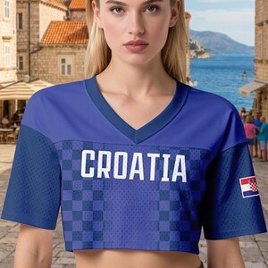 May include: A cropped blue jersey with the word "CROATIA" in white block letters. The jersey has a V-neck and a checkered pattern on the front. A Croatian flag patch is on the right sleeve.