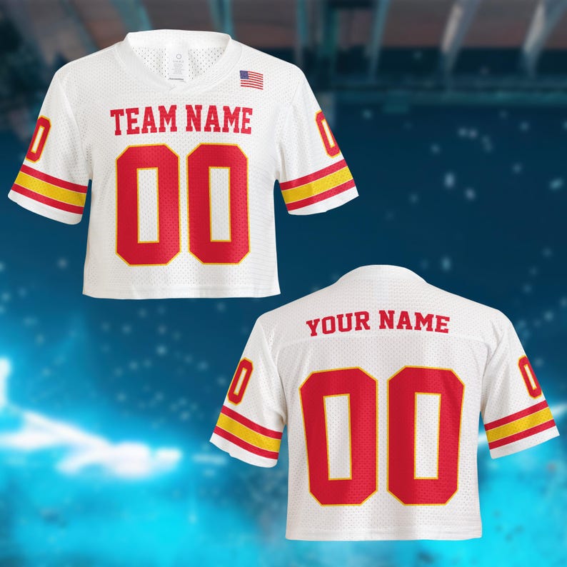 May include: White mesh jersey with red and yellow accents. The jersey features the text "TEAM NAME" and the number "00" in red. An American flag is visible on the upper right chest. A second jersey is visible with the text "YOUR NAME" and the number "00".