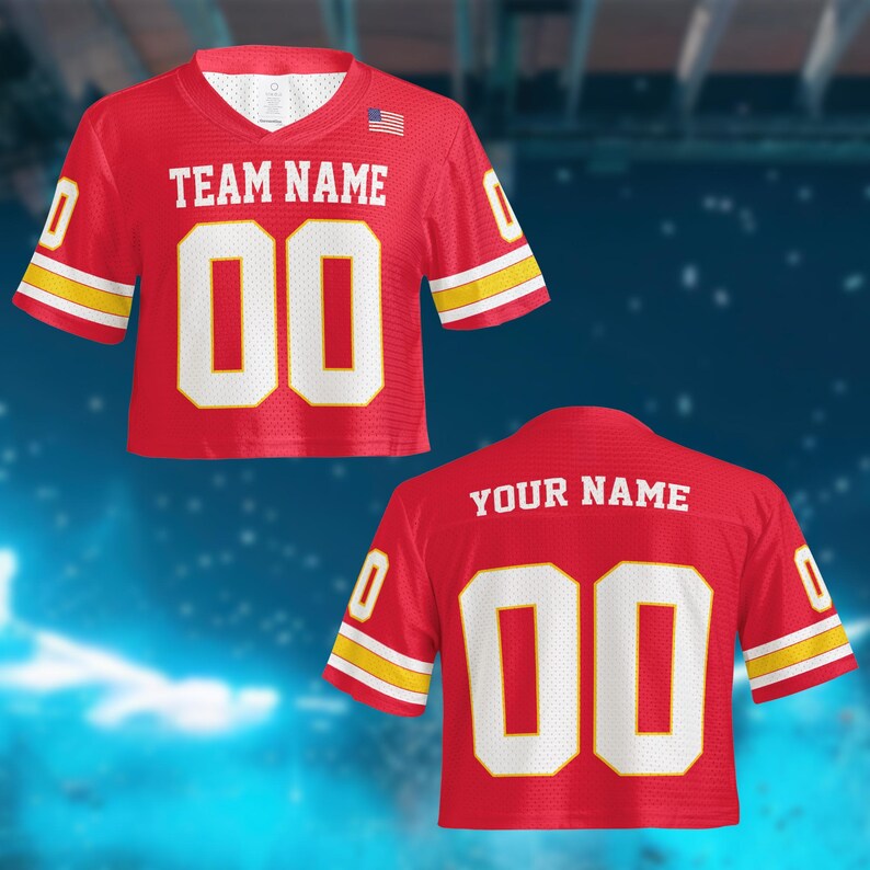 May include: Red cropped jersey with white numbers and lettering. The jersey has yellow and white stripes on the sleeves and features the text "TEAM NAME" and "00" on the front. The back of the jersey has the text "YOUR NAME" and "00". An American flag is visible.