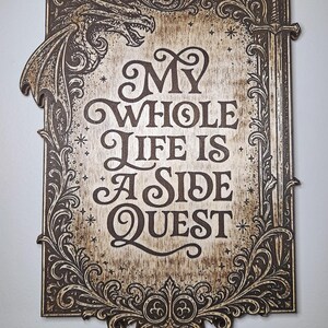 May include: Wooden sign with the text "My Whole Life Is A Side Quest" in a decorative font. The sign features a dragon, sword, and ornate border in dark brown against a light brown background.