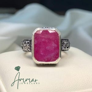 May include: A ring featuring a large, rectangular, faceted pink gemstone set in a silver band with intricate, dark, engraved scrollwork patterns on the sides. The text Ammar Jewellers is visible in the lower left corner of the image.