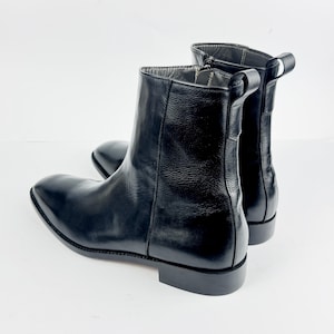 May include: A pair of black leather ankle boots with a pointed toe and a low heel. The boots have a side zip and a pull tab at the back. The boots are approximately 15 cm in height.