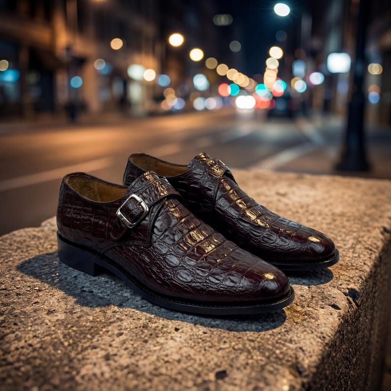 May include: A pair of dark brown leather dress shoes with a crocodile skin texture. The shoes have a buckle closure and are set on a stone surface with a blurred city street background.