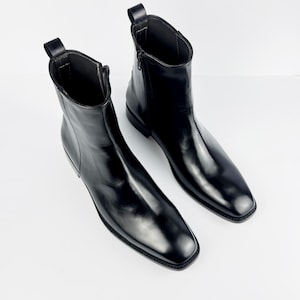May include: A pair of black leather ankle boots with a square toe and a side zip. The boots have a pull tab at the back and a low heel. The leather has a glossy finish.