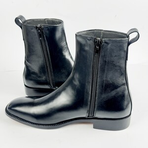 May include: A pair of black leather ankle boots. The boots feature a side zip, a small heel, and a pull tab. The leather has a glossy finish. The boots are set against a white background.