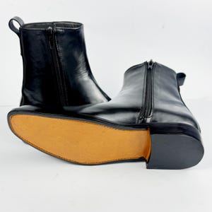 May include: A pair of black leather ankle boots with side zips. The boots have a rounded toe and a pull tab at the back. The soles are light brown.