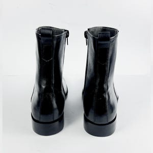 May include: A pair of black leather ankle boots. The boots have a shiny finish, a side zip, and a low block heel. The boots are shown from the back, against a white background.