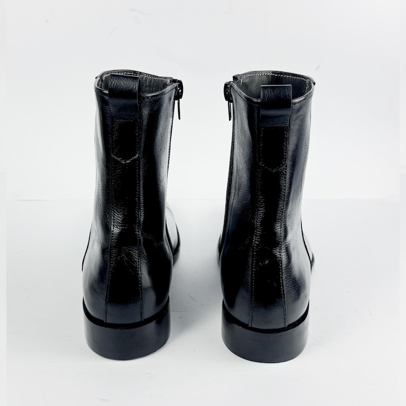 May include: A pair of black leather ankle boots. The boots have a shiny finish, a side zip, and a low block heel. The boots are shown from the back, against a white background.