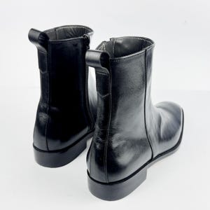 May include: A pair of black leather ankle boots with a square toe and a low heel. The boots have a side zip and a pull tab. The boots are approximately 15 cm tall.