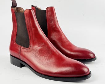 May include: A pair of red leather Chelsea boots with elastic side panels and a pull tab at the back. The boots have a low heel and a black sole. The boots are displayed on a white background.