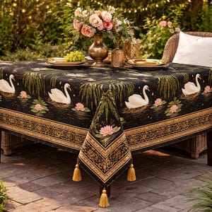 May include: A black tablecloth with a swan and lily pad design, gold trim, and tassels. The table is set with plates, a vase of flowers, and two wicker chairs. The scene is outdoors.
