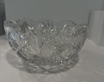 May include: A clear, cut-glass bowl with a scalloped rim. The bowl features intricate starburst and geometric patterns, creating a sparkling effect. The bowl is likely used for serving or display, adding elegance to any setting.