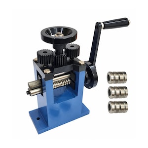 May include: A blue metal rolling mill machine featuring a black hand crank, a top adjustment wheel, and three exposed gears. The device includes two horizontal metal rollers and three separate cylindrical metal rollers with grooved surfaces.