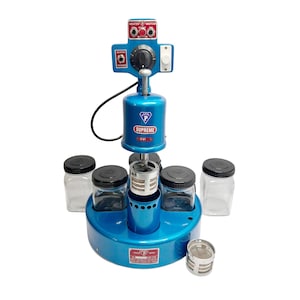 May include: A blue Supreme 110-VCL-5 watch cleaning machine with motor and heater controls. It features a central cleaning mechanism, four glass jars with black lids, and a separate metal filter. Designed for watch repair.