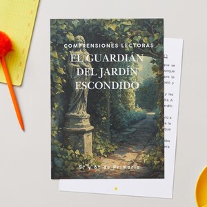 May include: A book cover with the title "EL GUARDIAN DEL JARDIN ESCONDIDO" featuring a statue in a garden setting. The cover is accompanied by a yellow notepad, an orange pen, a white paper, and a yellow cup.