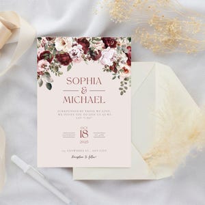 May include: A wedding invitation with the names "Sophia & Michael" in a serif font, adorned with floral arrangements in burgundy, cream, and green. The invitation includes the date "October 18, 2025" and is accompanied by a cream-colored envelope.