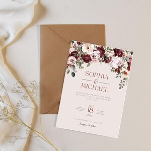 May include: A wedding invitation featuring the names "Sophia & Michael" in a serif font, adorned with burgundy and blush floral accents. The invitation includes the date "October 18, 2025" and is accompanied by a brown envelope.