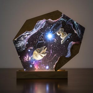 May include: An illuminated wooden art piece depicting a space scene with the Millennium Falcon and a TIE fighter. The artwork is set against a starry galaxy with a bright central light source.