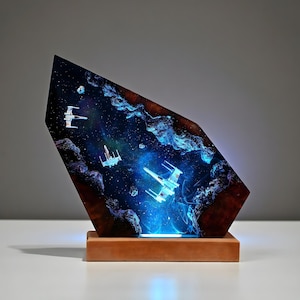May include: An illuminated resin art piece depicting a space scene with X-wing starfighters. The artwork is set within a dark blue and brown geometric shape, mounted on a wooden base. The piece has a blue light emanating from the base.