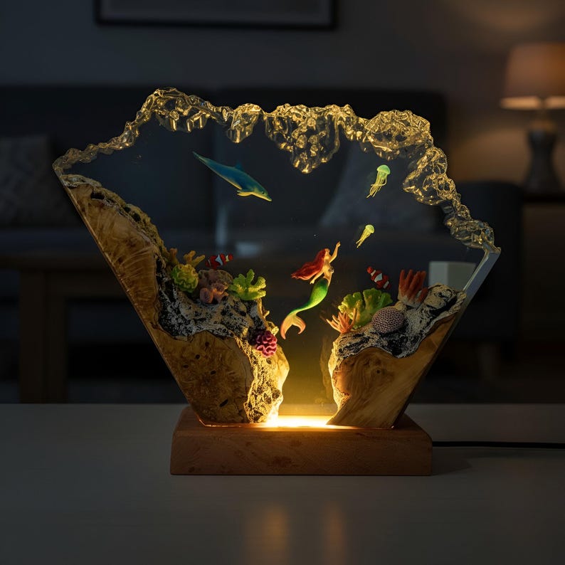 May include: A decorative lamp featuring an underwater scene with a mermaid, dolphin, and jellyfish. The lamp is encased in clear resin with a wooden base and accents. The lamp is illuminated with a warm, inviting glow.