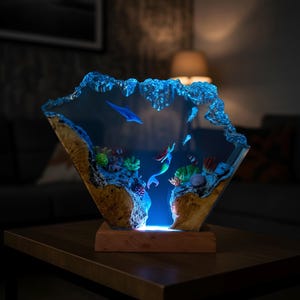May include: A decorative resin sculpture featuring an underwater scene with a mermaid, fish, and coral. The sculpture has a wooden base and a blue, glowing light. The edges are a textured, wave-like design.