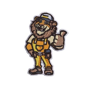 Puede incluir: Un parche bordado que muestra un león de dibujos animados con gorra de béisbol, camisa clara y peto amarillo con cinturón de herramientas. El león sonríe y hace un gesto de pulgar hacia arriba con una mano, en tonos marrón, amarillo y gris.