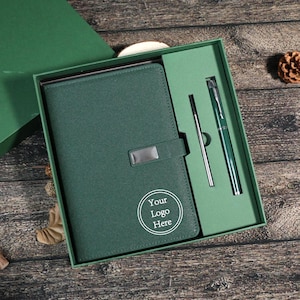 Puede incluir: Un juego de regalo verde que incluye un diario, un bolígrafo y un lápiz óptico. El diario tiene un cierre plateado y el texto "Your Logo Here" en un círculo blanco. El juego se presenta en una caja verde.