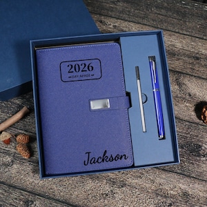 Puede incluir: Un juego de planificador diario azul 2026 en una caja de regalo. El planificador tiene un cierre plateado y el nombre "Jackson" impreso en la portada. El juego incluye un bol&iacute;grafo azul y una recarga de bol&iacute;grafo plateada.