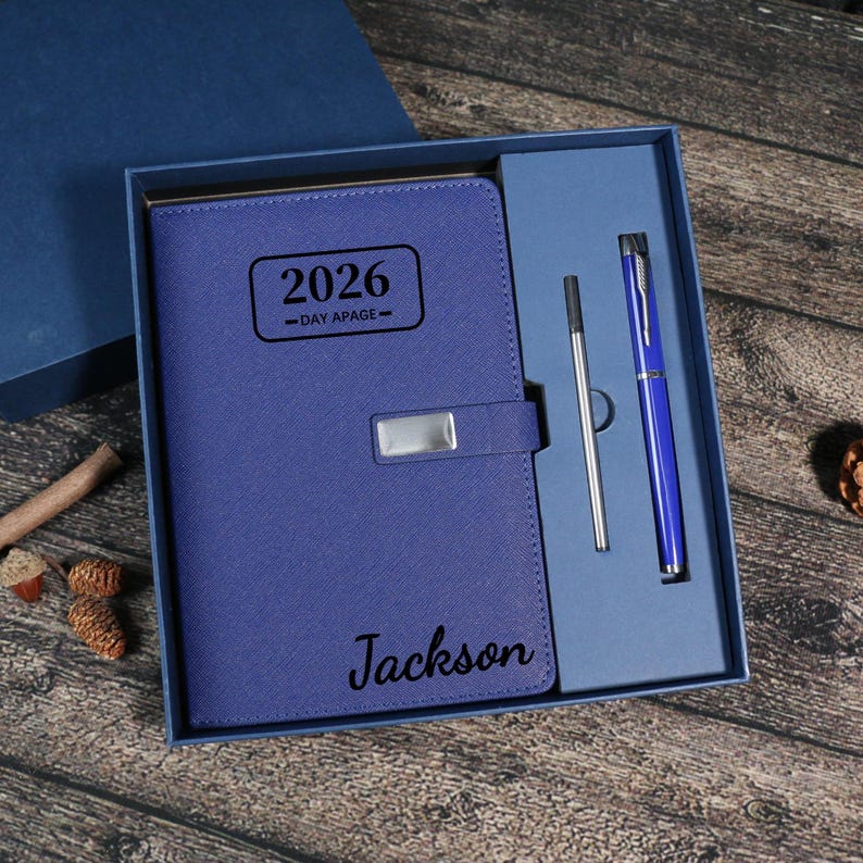 Puede incluir: Un juego de planificador diario azul 2026 en una caja de regalo. El planificador tiene un cierre plateado y el nombre "Jackson" impreso en la portada. El juego incluye un bol&iacute;grafo azul y una recarga de bol&iacute;grafo plateada.
