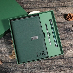 Könnte beinhalten: Ein grünes Geschenkset mit einem Notizbuch, einem Stift und einem Druckbleistift. Das Notizbuch hat einen silbernen Verschluss und die Initialen "L|K" sind auf dem Einband eingeprägt. Ein stilvolles und praktisches Geschenk.