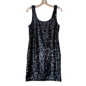 May include: A sleeveless black dress completely covered in small, reflective sequins. The garment features a wide scoop neckline and a straight, shift-style silhouette that hangs from a clear plastic hanger against a plain white background.