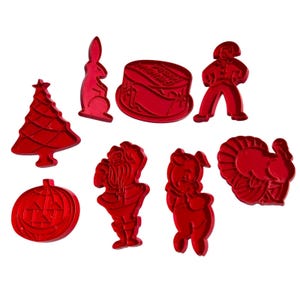Puede incluir: Un conjunto de cortadores de galletas de plástico rojo con diversas formas: un árbol de Navidad, un conejo, un pastel, una persona, una calabaza, Papá Noel, un cerdo y un pavo. Perfectos para hacer galletas festivas.