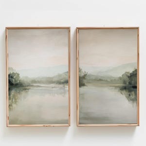 Puede incluir: Dos cuadros rectangulares verticales en marcos de madera clara, cada uno representando un paisaje sereno con un lago tranquilo, árboles de color verde suave y colinas distantes bajo un cielo pálido y tenue, formando un conjunto díptico coherente.