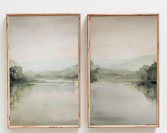 May include: Two vertical rectangular wall art prints in light wood frames, each depicting a serene landscape with a calm lake, soft green trees, and distant rolling hills under a pale, muted sky, creating a cohesive diptych set.
