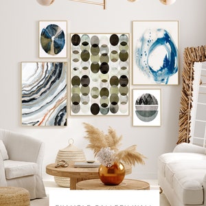 May include: A gallery wall featuring five abstract art prints in various shades of blue, green, and gray. The prints are arranged in a staggered pattern on a white wall. The prints are framed in gold.