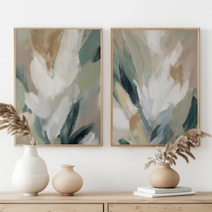 Puede incluir: Dos láminas de arte mural rectangulares con pinceladas abstractas en tonos verde salvia, crema, blanco y bronceado. Las obras están en marcos de madera clara, sobre un jarrón blanco y un jarrón color canela con hierba de la pampa seca.