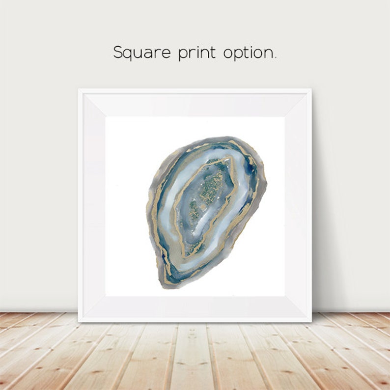 May include: Square framed print featuring a watercolor geode design. The geode has layers of blue, gray, and gold, with a sparkling center. The print is displayed on a white background with the text "Square print option."